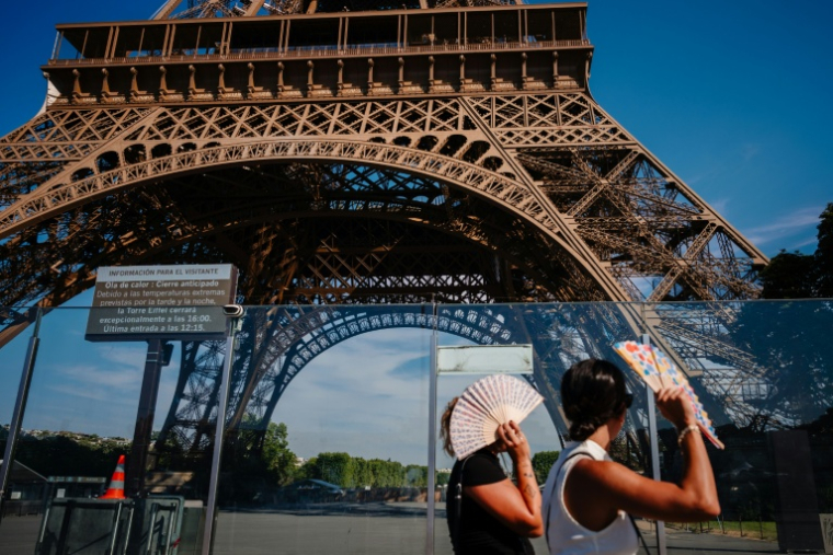 Des touristes se protègent du soleil avec des éventails en passant devant la tour Eiffel, fermée plus tôt en raison de la canicule, le 11 juillet 2026 à Paris ( AFP / Dimitar DILKOFF )