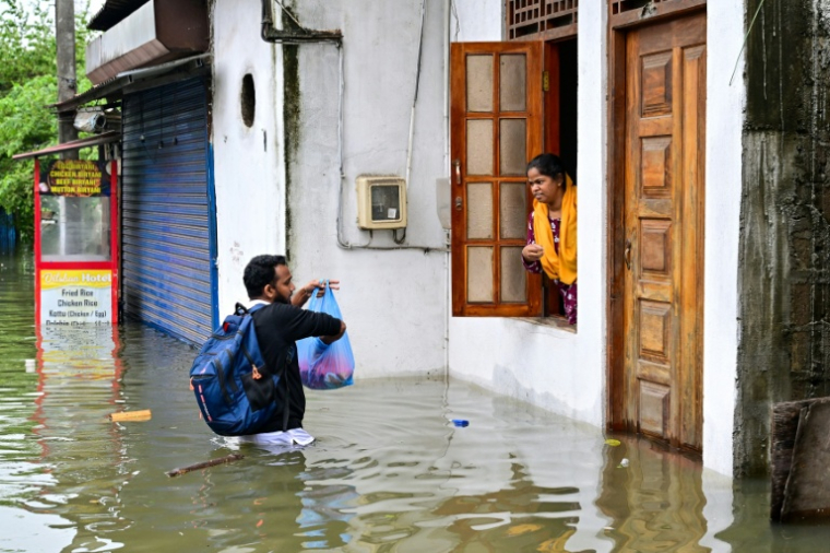 Un homme vient en aide à une femme bloquée dans une maison partiellement submergée, dans une zone inondée de Wellampitiya, en périphérie de Colombo, le 29 novembre 2025 au Sri Lanka ( AFP / Ishara S. KODIKARA )