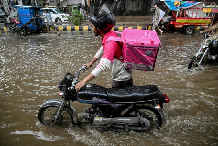 Abdullah Abbas, livreur de repas, pousse sa moto dans une rue inondée après de fortes pluies à Lahore, le 30 août 2025 au Pakistan ( AFP / Aamir QURESHI )