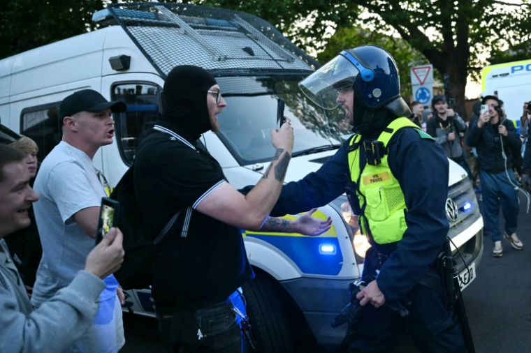 Des manifestants font face à un policier lors d'un rassemblement dans le centre d'Epping, au nord-est de Londres, le 20 juillet 2025 ( AFP / JUSTIN TALLIS )