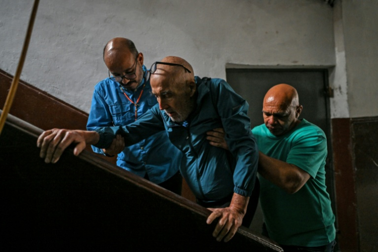 José Breijo est aidé pour monter les escaliers d'un immeuble résidentiel à Caracas, le 26 mai 2026 au Venezuela ( AFP / Juan BARRETO )