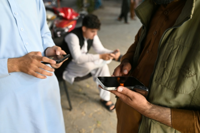 Des Afghans consultent leurs téléphones portables, le 1er octobre 2025 à Kaboul ( AFP / Wakil KOHSAR )