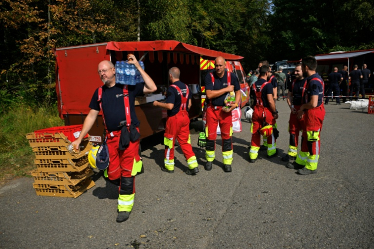 Des pompiers se servent en eau et en nourriture auprès d'un véhicule de soutien logistique des services d'incendie avant de partir lutter contre un feu dans le parc naturel des Hautes Fagnes, le 16 août 2026 à Baelen, dans l'est de la Belgique  ( AFP / JOHN THYS )