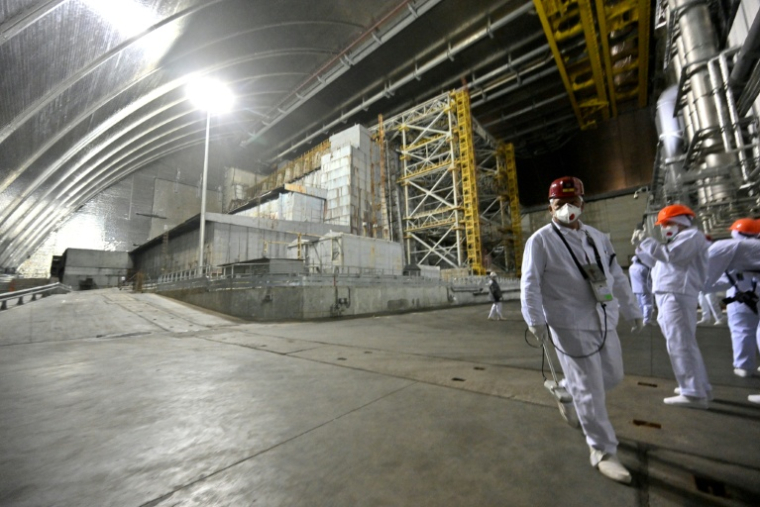 Des employés et des visiteurs marchent devant le sarcophage recouvrant le réacteur 4 détruit, sous la nouvelle enceinte de confinement dans la centrale nucléaire de Tchernobyl, le 24 avril 2026 ( AFP / Sergei SUPINSKY )