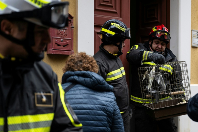Des pompiers sortent le 29 janvier 2026 des perroquets d'une maison évacuée après l'effondrement d'un long pan de falaise à Niscemi, petite ville de Sicile ( AFP / MARCO BERTORELLO )