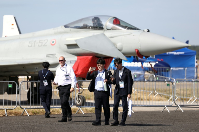 Des délégués devant un Eurofighter Typhoon de l'armée de l'air italienne lors de la journée d'ouverture du salon aéronautique international de Farnborough, au sud-ouest de Londres, le 20 juillet 2026 ( AFP / Toby Shepheard )