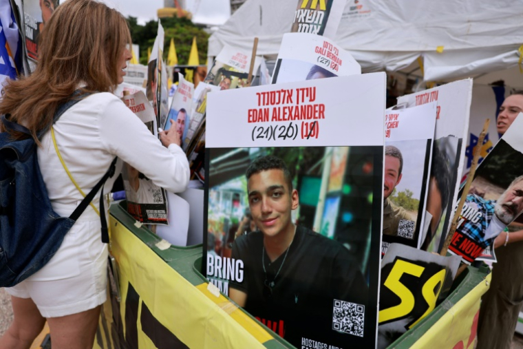 Une femme regarde des portraits d’otages israéliens détenus dans la bande de Gaza, dont un au centre représentant l’otage israélo-américain Edan Alexander, dont la libération est attendue le 12 mai 2025, sur la place des otages à Tel-Aviv, le 12 mai 2025 ( AFP / Menahem KAHANA )