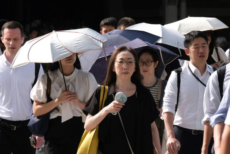Une femme, un ventilateur miniature à la main, se rend au travail par une matinée chaude et ensoleillée à Tokyo, le 6 août 2025 au Japon ( AFP / Kazuhiro NOGI )