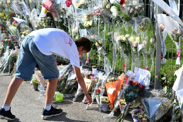 Un jeune homme dépose des fleurs devant les grilles du collège Françoise-Dolto, en hommage à Mélanie, la surveillante tuée par un élève, avant une marche silencieuse à Nogent, le 13 juin 2025 en Haute-Marne ( AFP / FRANCOIS NASCIMBENI )