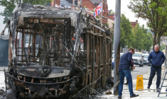Nettoyage de la rue à côté d'un bus calciné après des manifestations qui ont dégénéré en violences la nuit précédente, dans l'est de Belfast, en Irlande du Nord, le 10 juin 2026 ( AFP / Paul Faith )