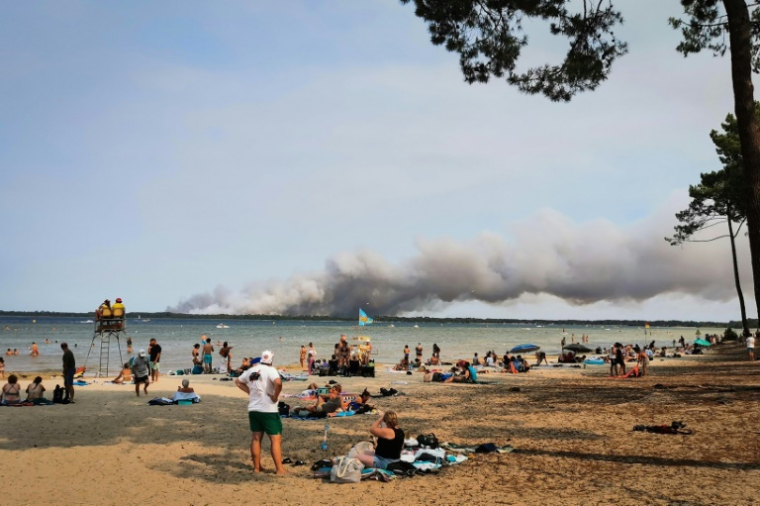 Des vacanciers sont assis sur la plage de Biscarrosse (sud-ouest), tandis qu'un épais nuage de fumée provoqué par un incendie s'élève dans le ciel, le 23 juillet 2026 ( AFP / Maximilien LAMY )