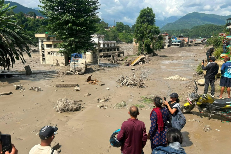 Des habitants observent des maisons partiellement submergées dans des eaux boueuses à la suite d'inondations soudaines survenues à Trishuli Bazar, dans le district de Nuwakot au Népal, le 26 août 2026. ( AFP / Prakash MATHEMA )