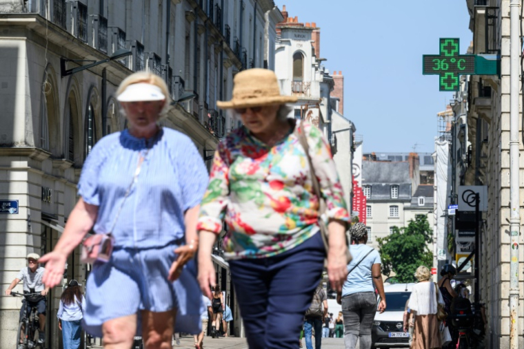 Des passants marchent dans une rue de Nantes alors qu'un thermomètre de pharmacie affiche 36 degrés, le 19 juin 2025 ( AFP / Loic VENANCE )
