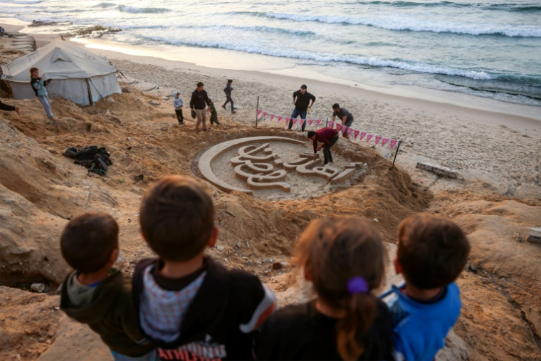 Des enfants regardent une sculpture de sable proclamant "Bienvenue au ramadan", le 17 février 2026 sur une plage au sud de la bande de Gaza ( AFP / Bashar Taleb )