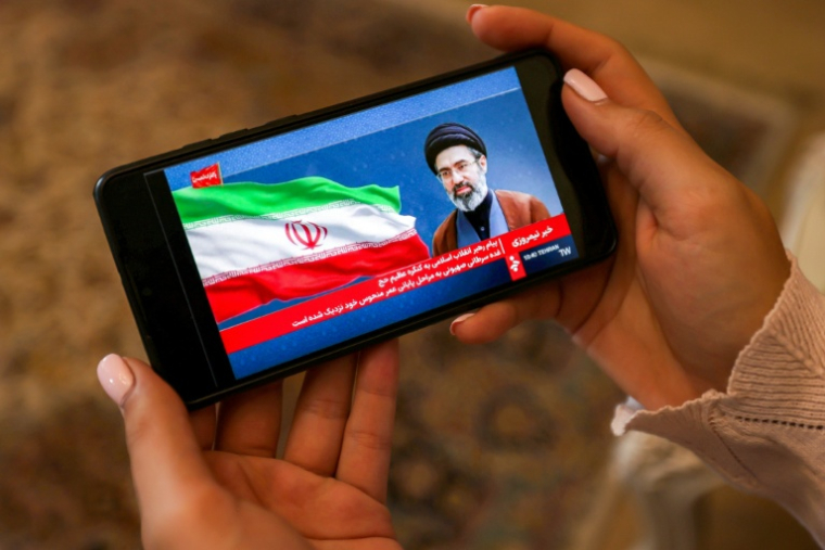 Une femme consulte sur son mobile un message du guide suprême iranien Mojtaba Khamenei, le 26 mai 2026 à Téhéran ( AFP / ATTA KENARE )