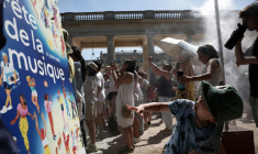 PDes piétons se rafraîchissent sous un brumisateur installé par la mairie de Paris à l'occasion de la 45e édition de la Fête de la Musique à Paris, pendant un épisode de canicule en France,  le 21 juin 2026 ( AFP / Guillaume BAPTISTE )