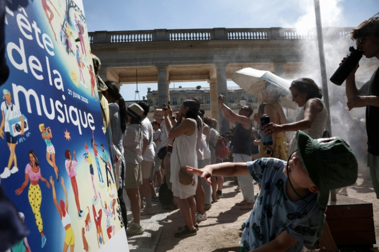 PDes piétons se rafraîchissent sous un brumisateur installé par la mairie de Paris à l'occasion de la 45e édition de la Fête de la Musique à Paris, pendant un épisode de canicule en France,  le 21 juin 2026 ( AFP / Guillaume BAPTISTE )