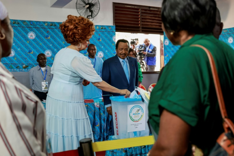 Le président camerounais sortant Paul Biya (G) regarde son épouse Chantal glisser son bulletin dans l'urne dans un bureau de vote  à Yaoundé, le 12 octobre 2025 ( AFP / Daniel BELOUMOU OLOMO )