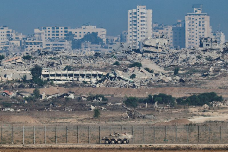 Un véhicule blindé de transport de troupes manœuvre le long du côté israélien de la frontière, tandis que la destruction à Gaza est visible