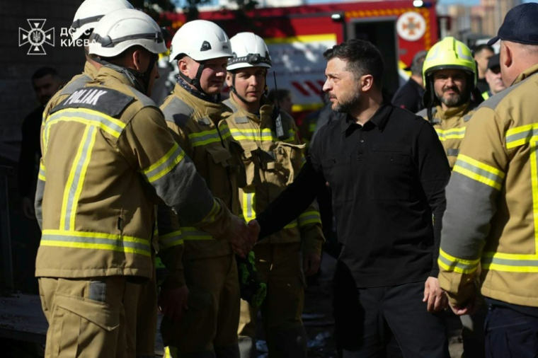 Photo prise et diffusée par les services d'urgence ukrainiens, le 15 mai 2026, montrant le président ukrainien Volodymyr Zelensky (c) rencontrant des secouristes ukrainiens sur le site d'une attaque aérienne à Kiev ( UKRAINIAN EMERGENCY SERVICE / Handout )