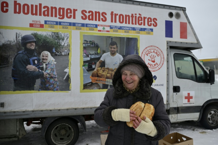 Une femme réagit en tenant des pains fraîchement cuits distribués par le boulanger bénévole français Loïc Nervi depuis sa boulangerie mobile à Borodianka, dans la région de Kiev, le 19 février 2026, dans le contexte de l'invasion russe de l'Ukraine. ( AFP / Genya SAVILOV )