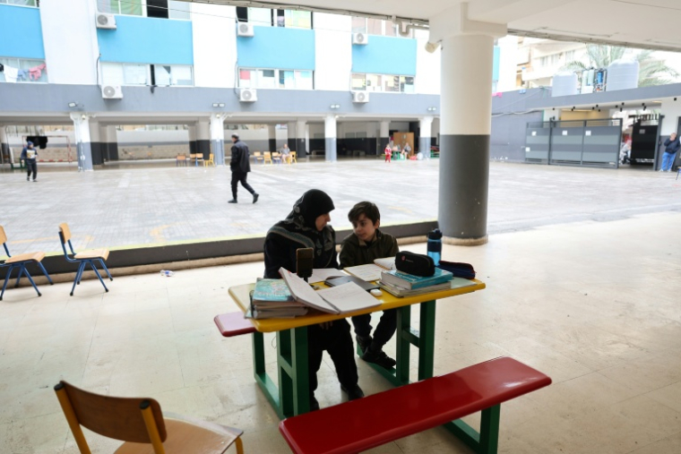 Une femme, assise à côté d'un enfant, supervise ses études en ligne sur un téléphone portable dans une école publique transformée en refuge pour personnes déplacées, à Dekwaneh, au nord de Beyrouth, le 25 mars 2026 au Liban ( AFP / Anwar AMRO )