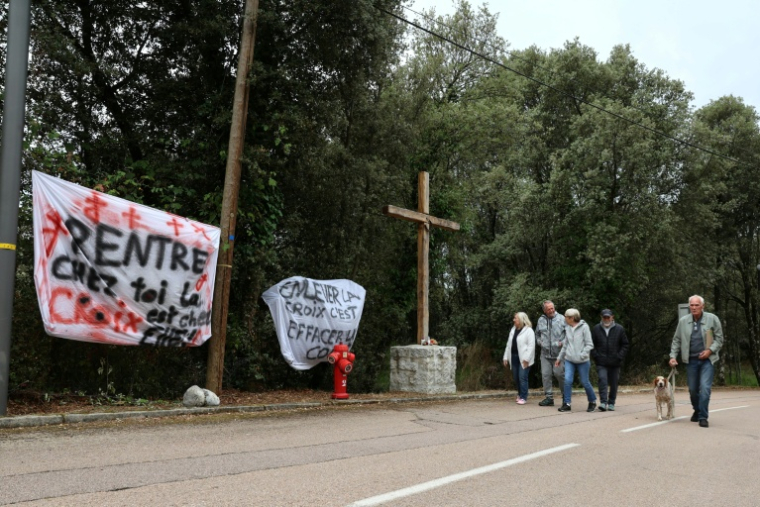 Des banderoles à côté d'une croix en bois objet de polémiques à l'entrée du village de Quasquara, le 14 octobre 2025 en Corse-du-Sud ( AFP / Pascal POCHARD-CASABIANCA )