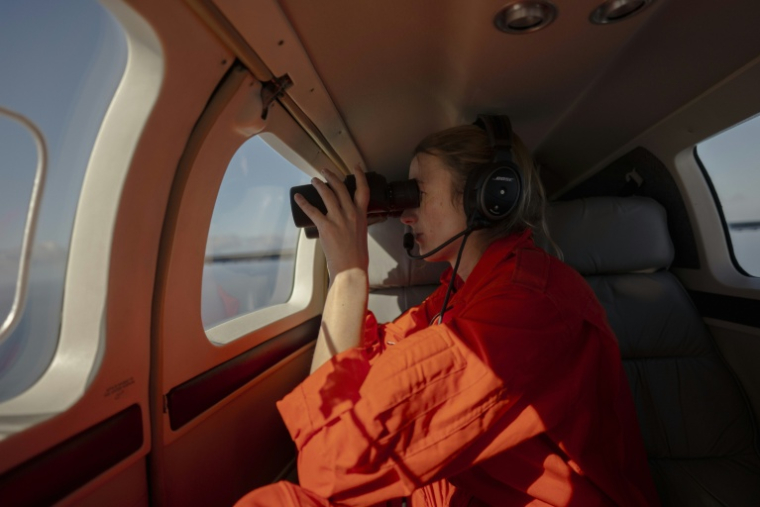 Une membre de l'ONG Humanitarian Pilots Initiative (HPI) observe l'océan Atlantique à la recherche d'embarcations de migrants en détresse, le 22 janvier 2026 ( AFP / MICHELE CATTANI )