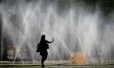 Une femme prend une photo de tuyaux d'arrosage déversant de l'eau pour apporter un peu de fraîcheur face à la chaleur estivale, à Cologne, dans l'ouest de l'Allemagne, le 25 juin 2026 ( AFP / Ina FASSBENDER )
