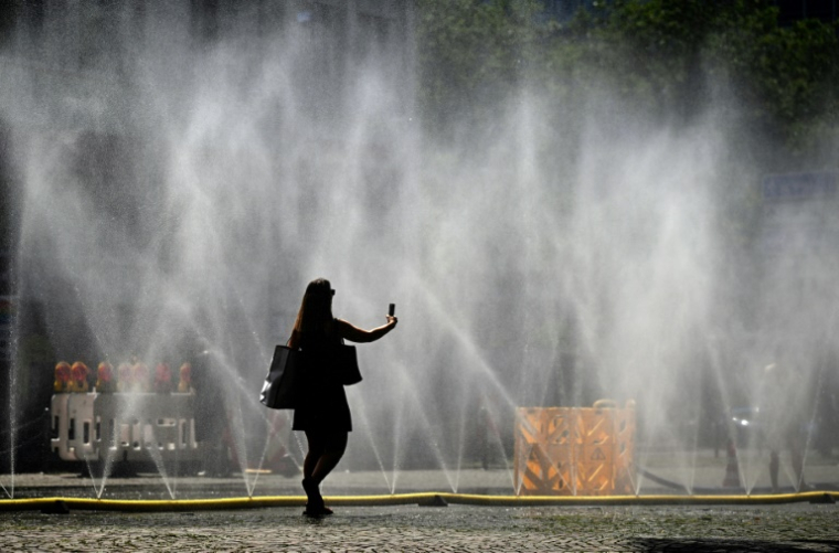 Une femme prend une photo de tuyaux d'arrosage déversant de l'eau pour apporter un peu de fraîcheur face à la chaleur estivale, à Cologne, dans l'ouest de l'Allemagne, le 25 juin 2026 ( AFP / Ina FASSBENDER )