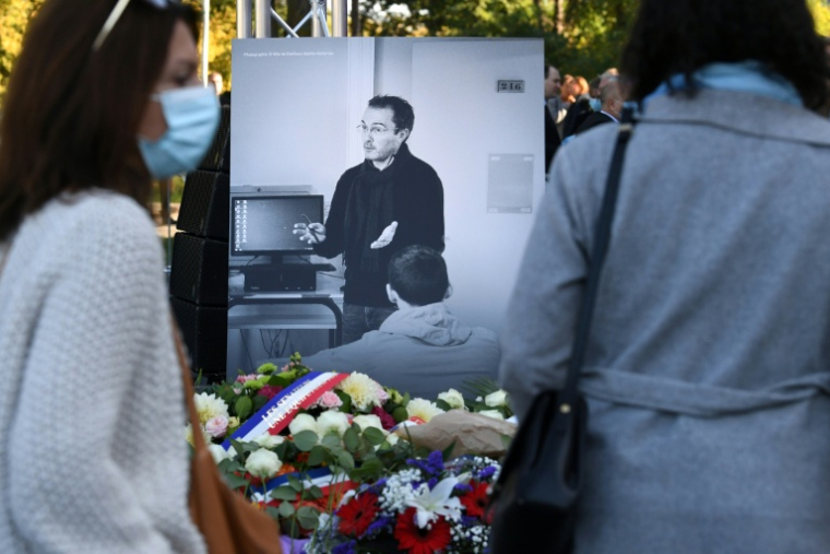 Des personnes passent devant une photographie de Samuel Paty lors d'une cérémonie hommage organisée à Eragny-sur-Oise, au nord-ouest de Paris, le 16 octobre 2021 ( AFP / Alain JOCARD )