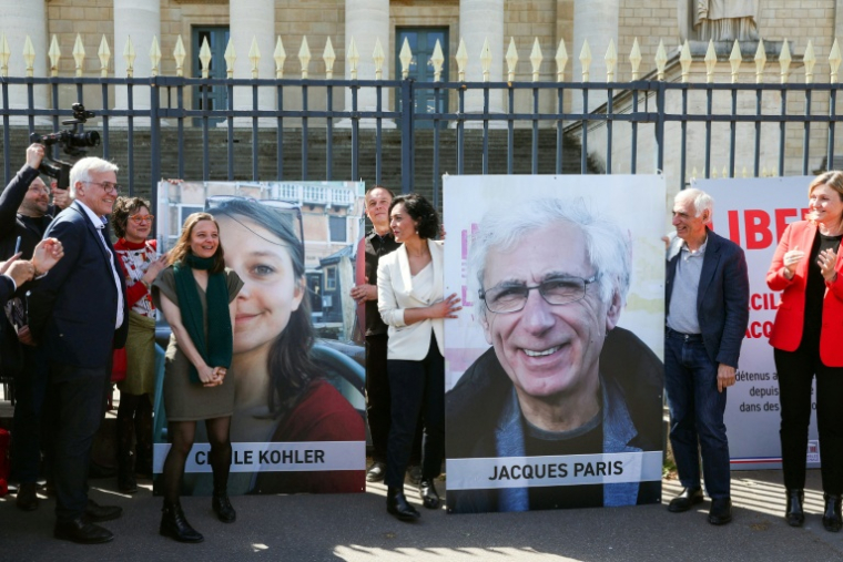Cécile Kohler (3e G) et Jacques Paris (2e D) devant leurs portraits décrochés des grilles de l'Assemblée nationale, à Paris le 14 avril 2026 ( AFP / ALAIN JOCARD )