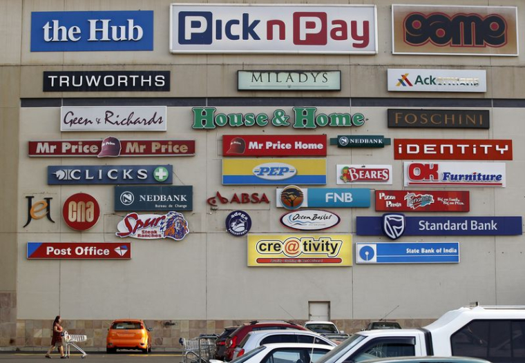 Un client pousse son chariot alors que des logos de magasins sont affichés sur un mur du centre commercial de Lenasia, au sud de Johannesburg