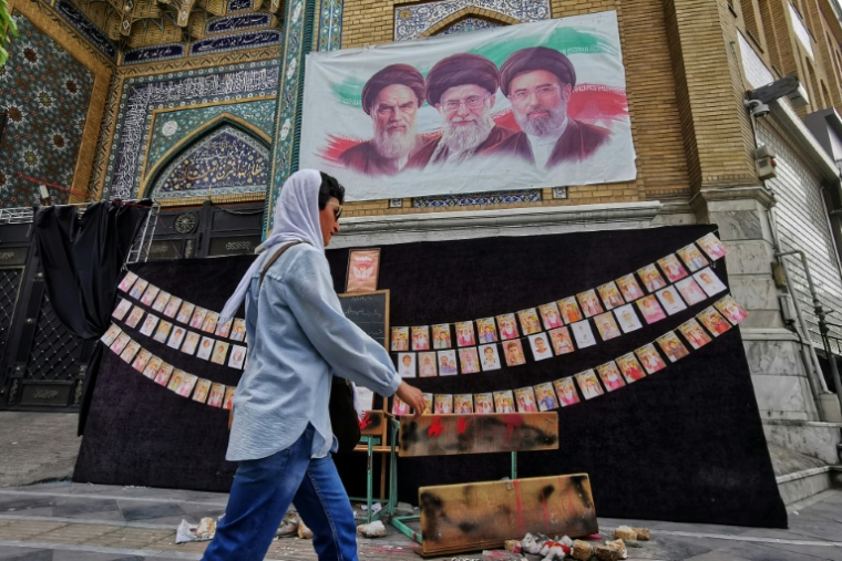 Une passante marche à côté des portraits des trois guides suprêmes de l'histoire de la République islamique d'Iran, l'ayatollah Rouhollah Khomeini, l'ayatollah Ali Khamenei et Mojtaba Khamenei (de gauche à droite), et de photos d'enfants tués lors du bombardement de l'école de Minab en février, le 25 avril 2026 à Téhéran ( AFP / ATTA KENARE )