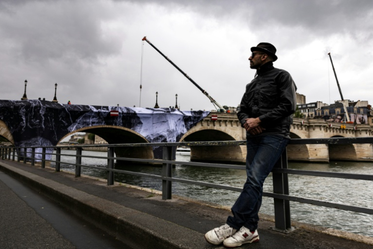 L'artiste français JR sur les quais de Seine devant le Pont Neuf qu'il entend traNsformer en "caverne", le 13 mai 2026 à Paris  ( AFP / Joel Saget )