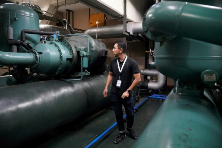 Un technicien de la société Recoolit travaille à capturer les gaz de refroidissemen d'une grande unité de climatisation au sous-sol d'un complexe d'habitation à Jakarta, le 10 juin 2025 en Indonésie ( AFP / Jack Moore )