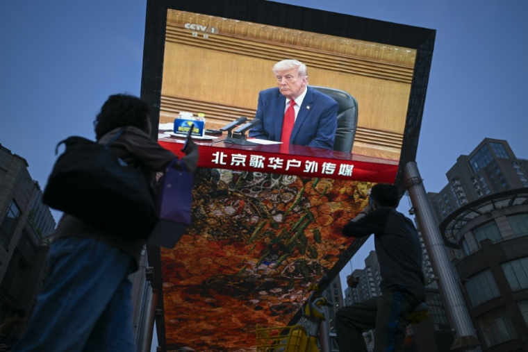 Des personnes passent devant un écran sur lequel est visible Donald Trump, le 14 mai 2026 à Pékin ( AFP / WANG Zhao )