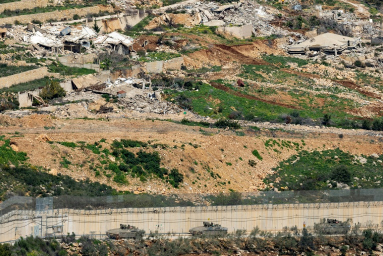 Des véhicules de combat de l'armée israélienne manœuvrent du côté israélien de la clôture frontalière, en face d'un village libanais détruit, vu de la Haute Galilée, dans le nord d'Israël, le 16 mars 2026 ( AFP / Odd ANDERSEN )