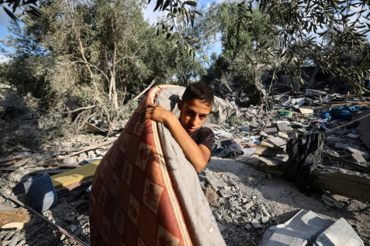 Un garçon palestinien récupère un matelas des décombres d'une maison après une frappe israélienne nocturne qui a touché Nousseirat, dans le centre de la bande de Gaza, le 13 juillet 2025 ( AFP / Eyad BABA )