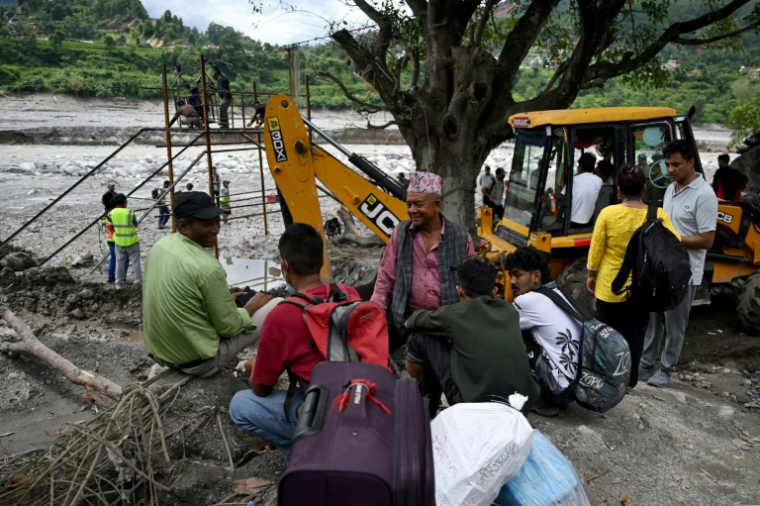 Des habitants regroupés près de la rivière Trishuli tandis que des ouvriers installent une tyrolienne au dessus du cours d'eau à Bidur au Népal le 2 septembre 2026 ( AFP / Arun SANKAR )