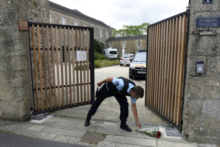 Un gendarme ramasse des fleurs à l'entrée de la communauté religieuse à Saint-Laurent-sur-Sevres, le 9 août 2021 ( AFP / Sebastien SALOM-GOMIS )