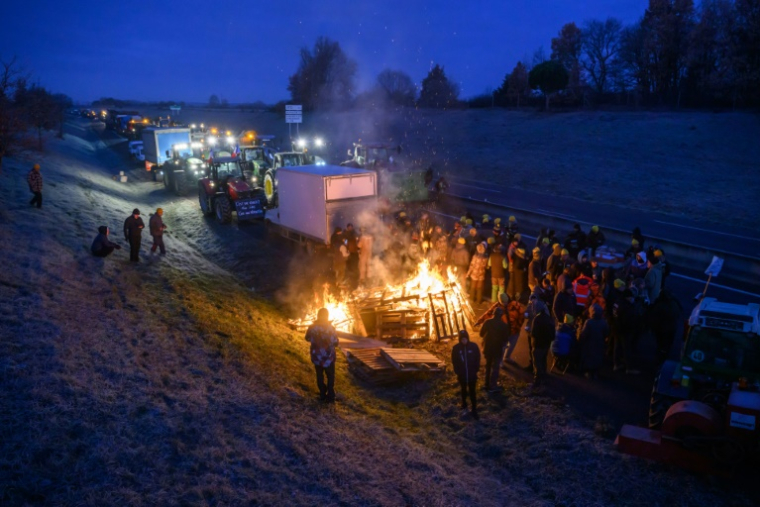 Des agriculteurs se réchauffent autour d'un feu alors qu'ils sont empêchés par les gendarmes d'entrer dans Toulouse dans le cadre de leur manifestation pour défendre leur profession et dénoncer la gestion de la crise agricole par le gouvernement, près de Leguevin, le 7 janvier 2026.  ( AFP / Ed JONES )