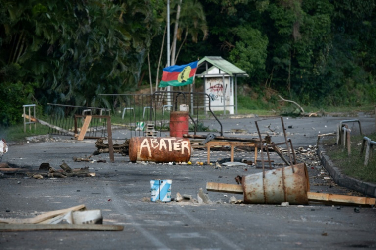 Un drapeau du FLNKS parmi des débris calcinés d'un barrage routier près de Mont-Dore, en périphérie de Nouméa, le 25 juin 2026 en Nouvelle-Calédonie ( AFP / Delphine Mayeur )
