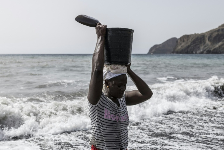 Vania Tavares porte en équilibre sur sa tête un seau rempli de sable noir, sur une plage dégradée par l'exploitation commerciale, près de Ribeira da Barca, le 20 mai 2026 au Cap-Vert ( AFP / PATRICK MEINHARDT )