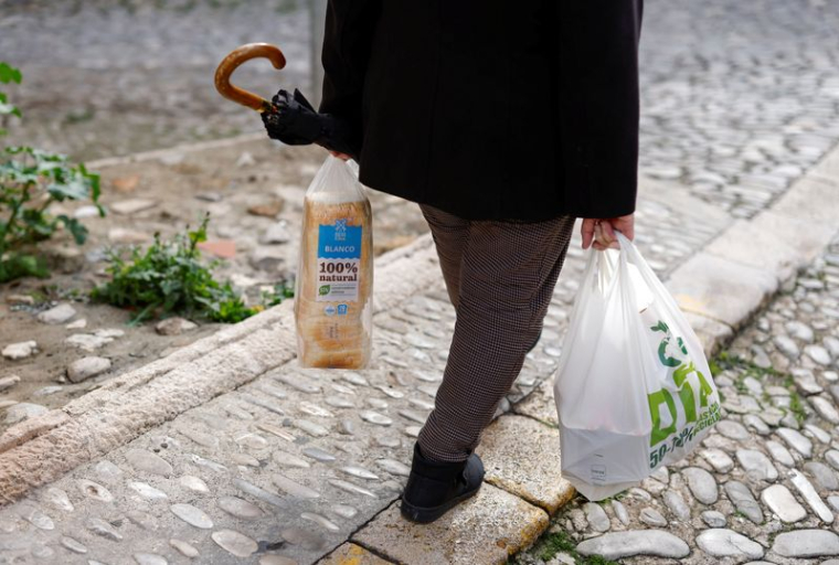 Une retraitée transporte un sac en plastique contenant des provisions et du pain tranché, alors qu'elle marche le long d'une rue à Ronda