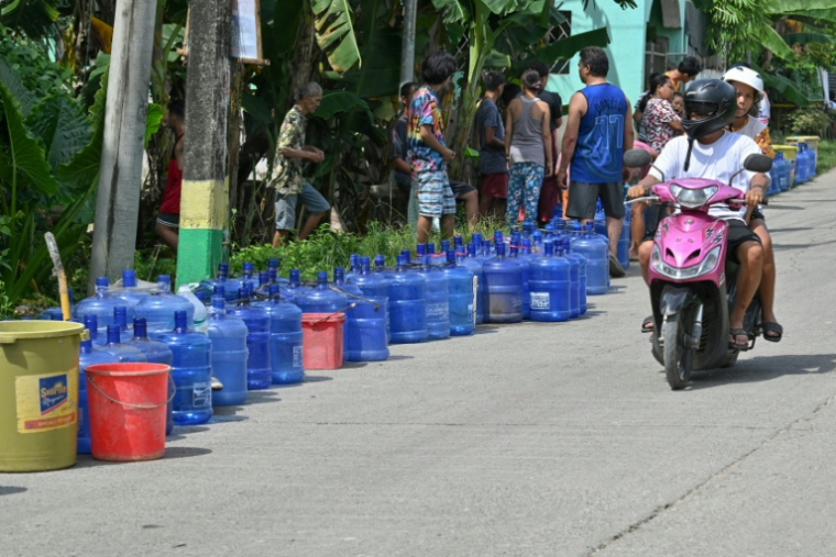 Une moto passe devant une file de bombonnes en plastique placées par des habitants qui attendent des livraisons d'eau dans la ville de Bogo, dans la province de Cebu aux Philippines, le 2 octobre 2025 ( AFP / TED ALJIBE )