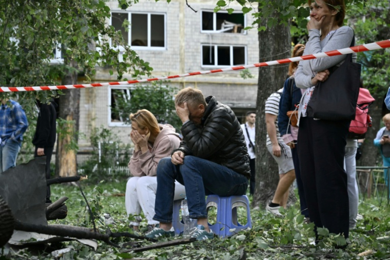 Des habitants en état de choc attendent pendant que des sauveteurs ukrainiens effectuent des recherche dans un immeuble résidentiel fortement endommagé par une frappe de missile russe, le 17 juin 2025 à Kiev ( AFP / Genya SAVILOV )