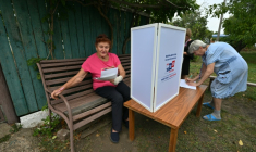 Une femme examine des bulletins de vote dans un bureau de vote mobile installé par les membres d'une commission électorale locale, accompagnés d'un militaire russe, à Novonikolayevka, dans la région de Donetsk, en Ukraine sous contrôle russe, le 14 septembre 2026 ( AFP / STRINGER )