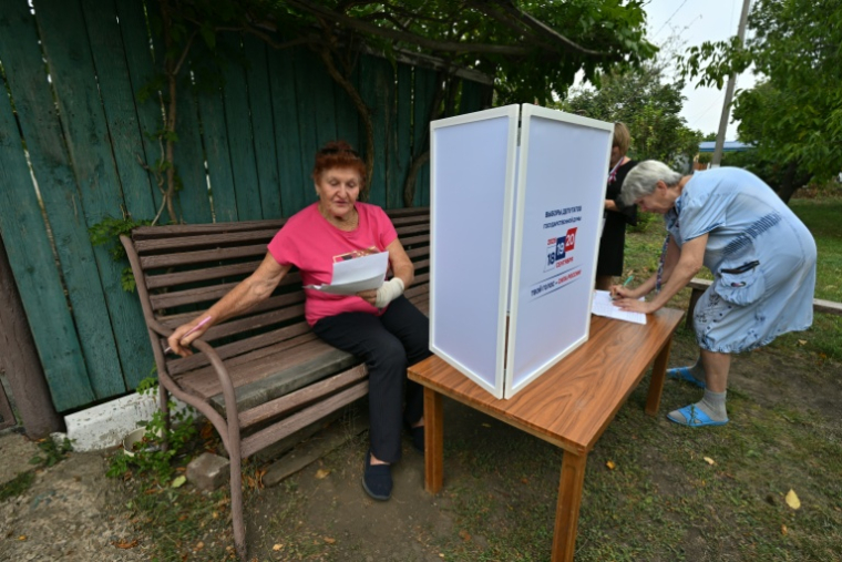 Une femme examine des bulletins de vote dans un bureau de vote mobile installé par les membres d'une commission électorale locale, accompagnés d'un militaire russe, à Novonikolayevka, dans la région de Donetsk, en Ukraine sous contrôle russe, le 14 septembre 2026 ( AFP / STRINGER )