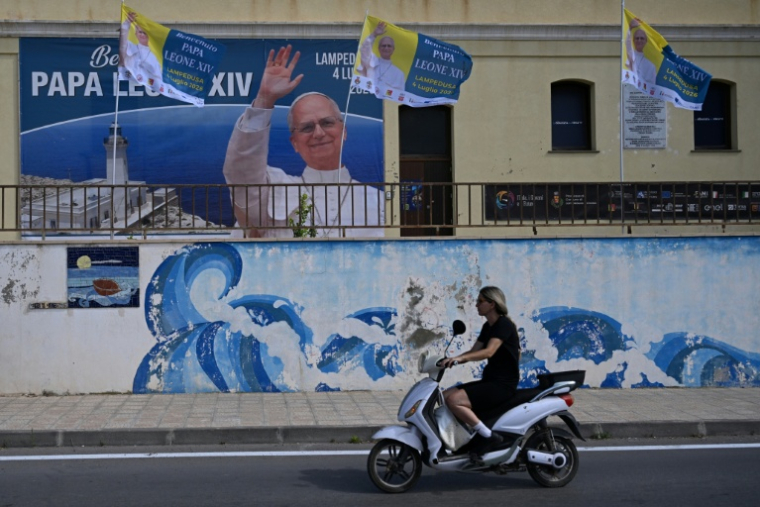 Une personne circule près d'une affiche posée pour la visite du pape Léon XIV, le 3 juillet 2026 à Lampedusa (Italie) ( AFP / Tiziana FABI )